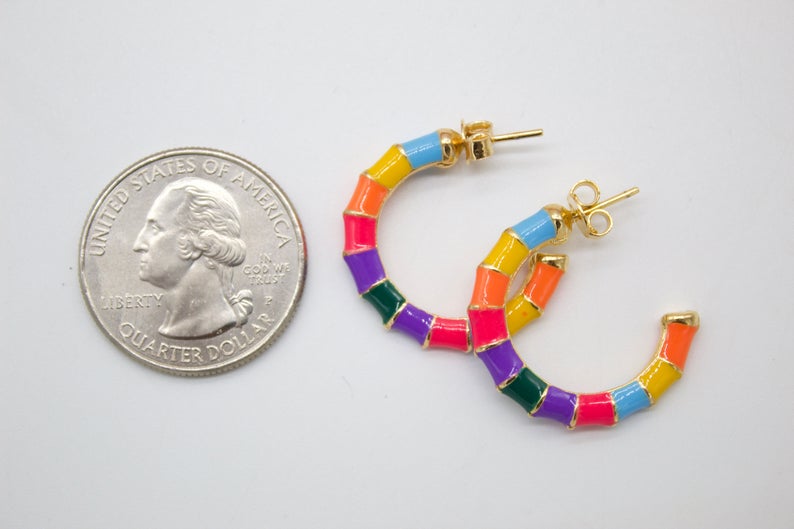 A pair of colorful, segmented rainbow hoop earrings rests next to a US quarter coin for scale.