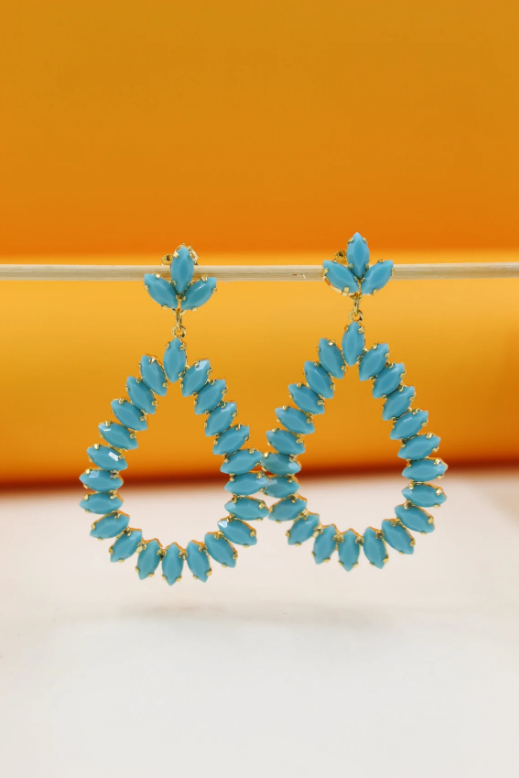 A pair of turquoise teardrop crystal earrings hangs delicately against an orange and white background.