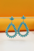 A pair of turquoise teardrop crystal earrings hangs delicately against an orange and white background.