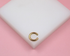 A shiny gold initial C ear cuff rests on a white display block against a soft pink background.