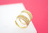 Two gold huggie hoop earrings encrusted with sparkling cubic zirconia crystals rest on a white surface against a bright pink background.