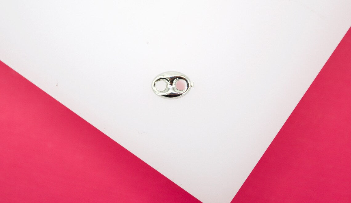 A polished silver can tab jewelry piece rests centrally on a white surface against a bright pink background.
