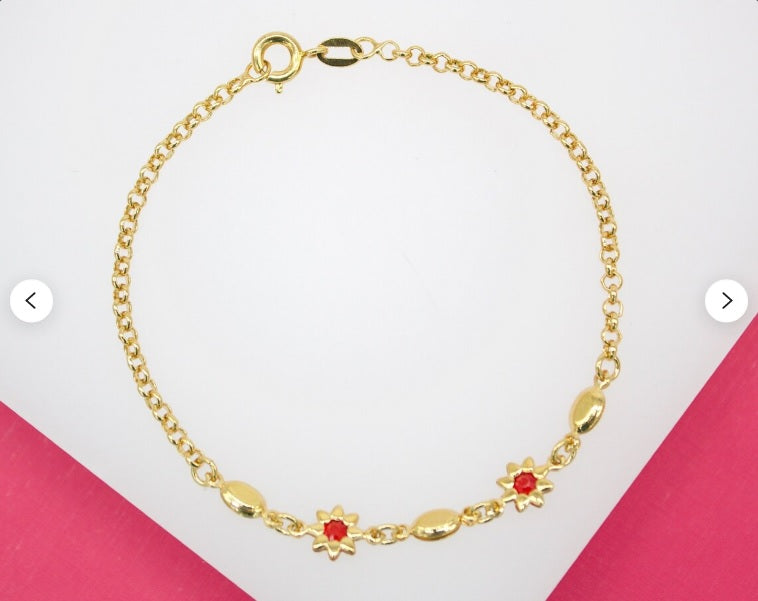 A delicate gold link bracelet features red flower charms and oval beads, displayed against a white and pink background.