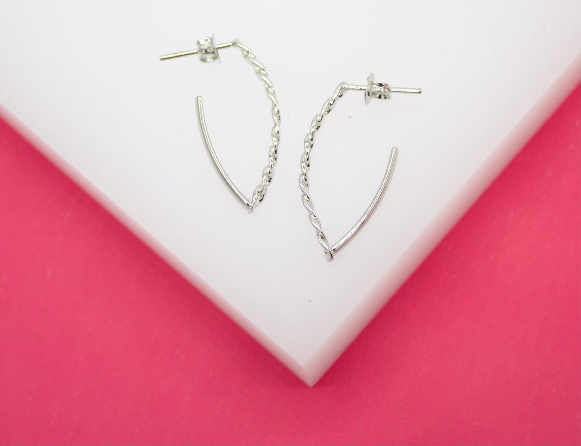 A pair of unique silver hoop earrings featuring a half-twisted design rests on a white display surface against a vibrant pink background.