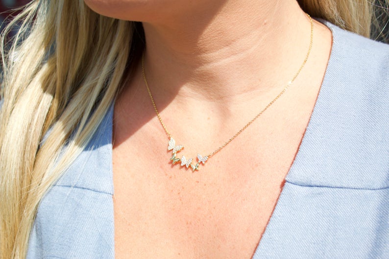 A blonde woman wearing a delicate gold butterfly pendant necklace.