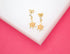 A pair of gold turtle earrings with orange shells and sparkling crystal accents rest on a white display surface against a vibrant pink background.