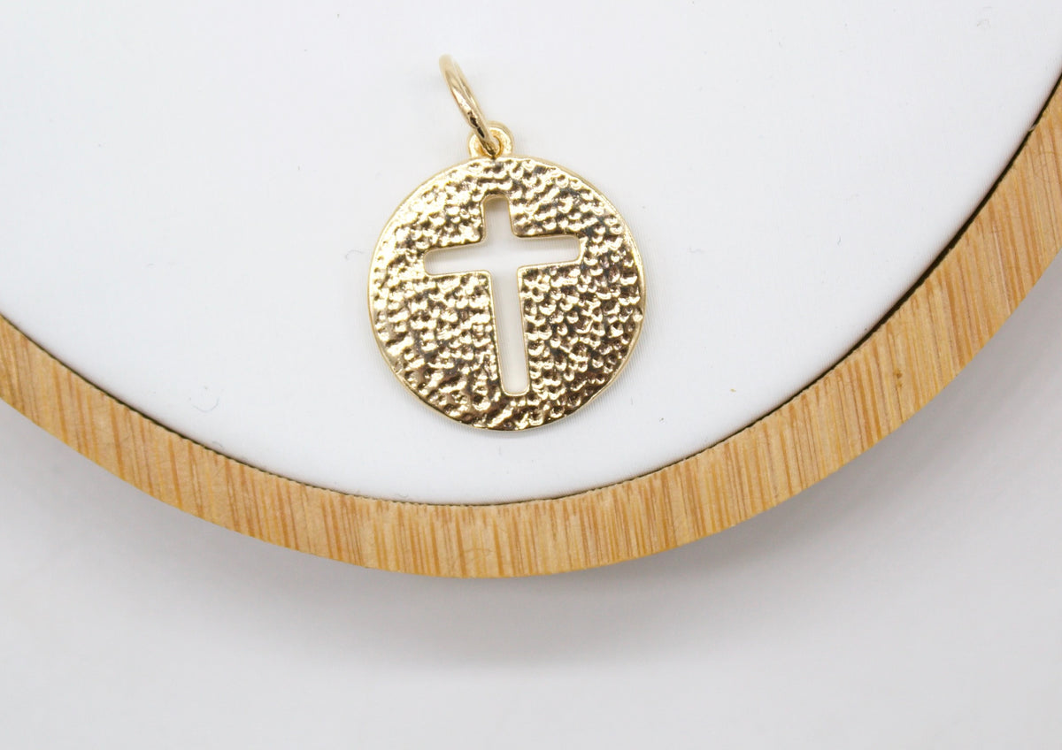 A gold textured circular pendant featuring a cutout cross rests on a white display tray.