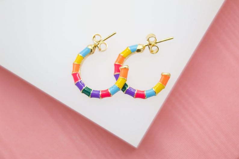 A pair of colorful enameled bamboo hoop earrings rests on a white and pink display surface.