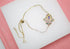 A delicate gold Hamsa hand bracelet features sparkling multicolored stones and a central blue evil eye charm against a neutral background.