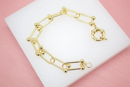 A polished gold paperclip link bracelet with round ball accents rests on a white display surface.