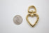 A shiny gold heart-shaped swivel lobster clasp rests next to a US quarter coin for scale on a white background.