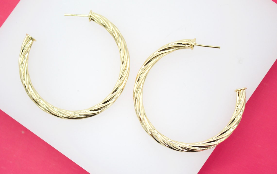 A pair of elegant twisted gold hoop earrings rests against a white and pink surface.