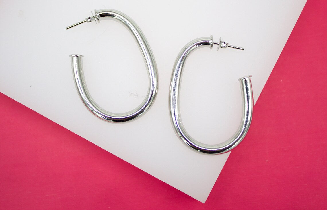 A pair of sleek silver hoop earrings rests on a white and pink background.
