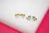 Two pairs of colorful unicorn earrings rest on a white display surface against a pink background.