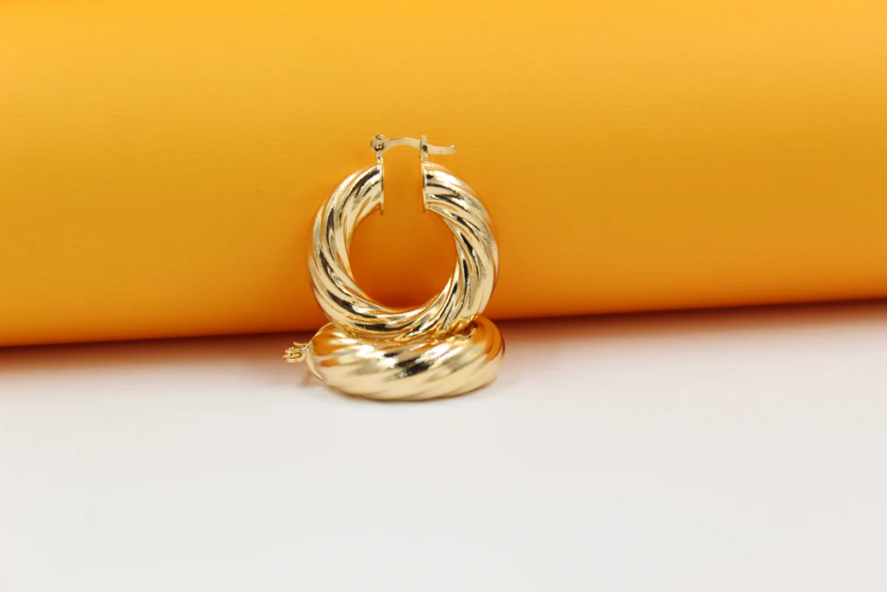 A pair of shiny gold twisted hoop earrings rests against a vibrant yellow and white backdrop.