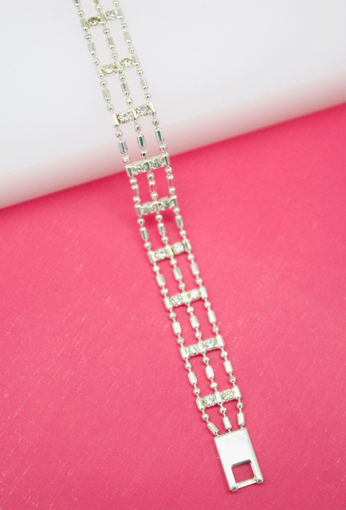 A delicate silver multi-strand rhinestone bracelet lies against a vibrant pink and white background.