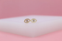 Two gold evil eye stud earrings with crystal centers rest on a white display against a pink background.