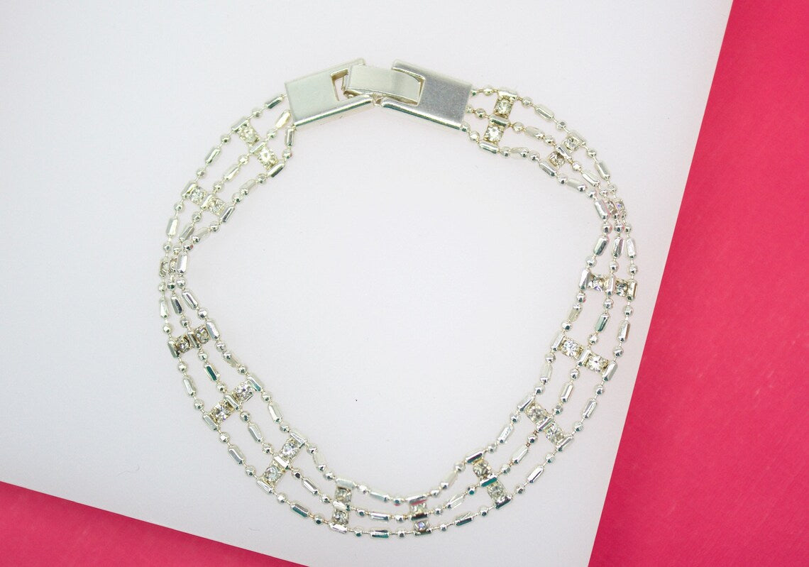 A multi-strand silver bracelet featuring sparkling rhinestones rests on a white and pink surface.