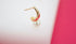 A gold and pink enamel hoop earring accented with a dangling white pearl rests against a white and pink background.