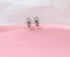 Two sleek, silver hoop earrings rest elegantly on a soft pink surface against a white paper background.