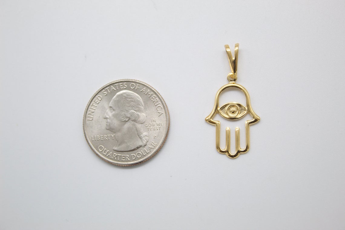 A gold Hamsa hand pendant rests next to a US quarter coin for size comparison.