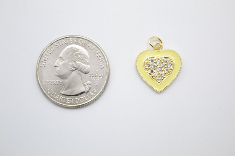 A shiny gold heart-shaped charm with yellow enamel and a pavé cubic zirconia center rests next to a US quarter coin for scale.