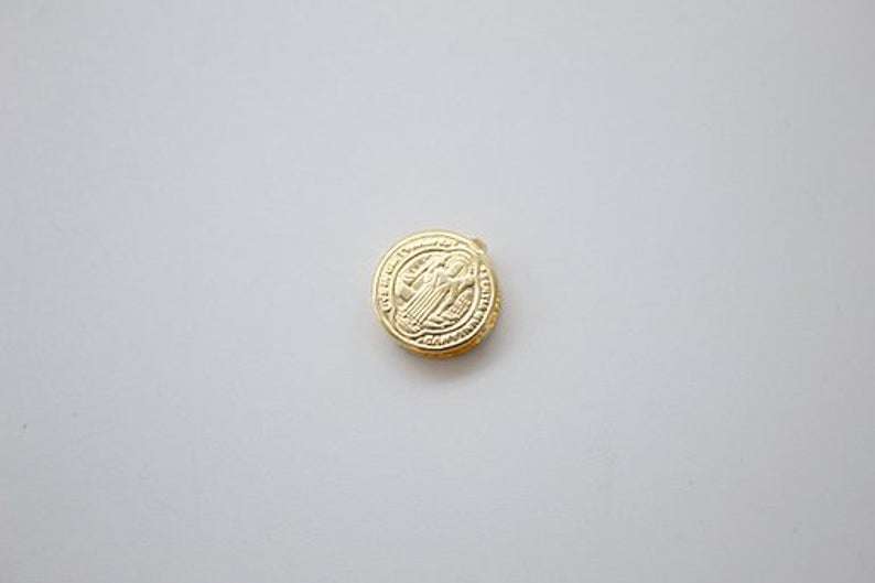 A small gold pendant coin rests flat against a clean white background.