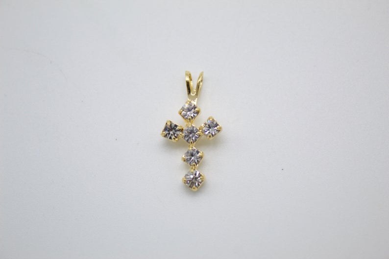 A delicate gold cross pendant features sparkling cubic zirconia stones set against a neutral background.