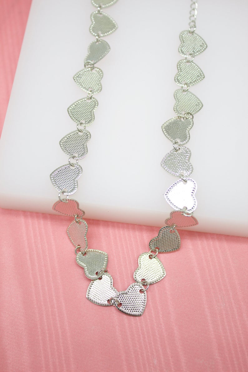 A delicate silver heart link necklace rests against a white and pink background.