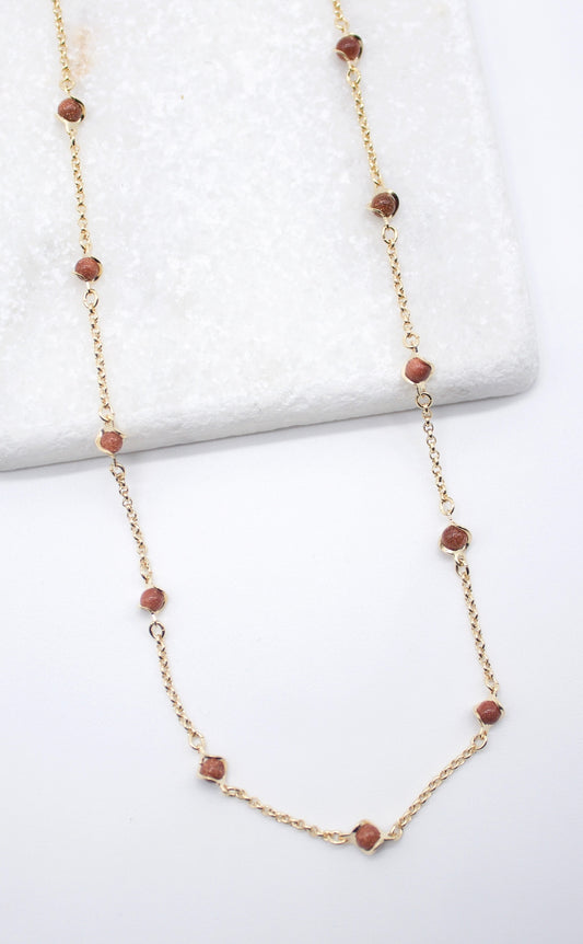 A delicate gold chain necklace featuring spaced brown gemstone beads rests against a white textured background.
