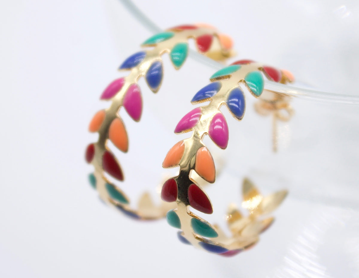 A pair of gold hoop earrings features vibrant enamel leaves in various colors.