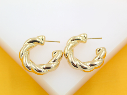 A pair of polished gold twist hoop earrings rests against a white and yellow background.