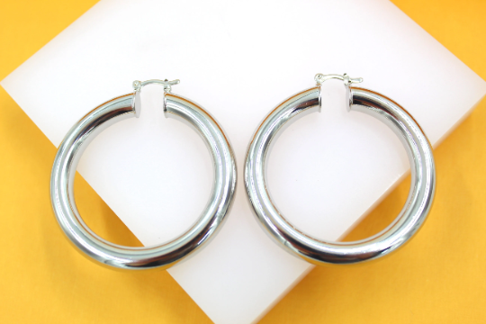 A pair of thick, polished silver hoop earrings rests on a white display against a bright yellow background.