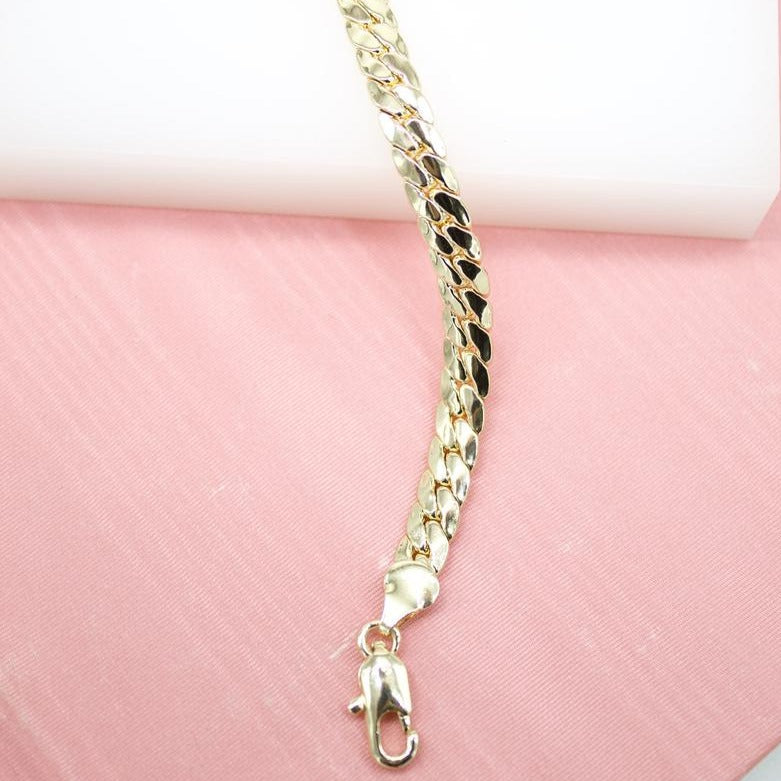 A shiny gold curb chain necklace rests on a pink surface against a white background.