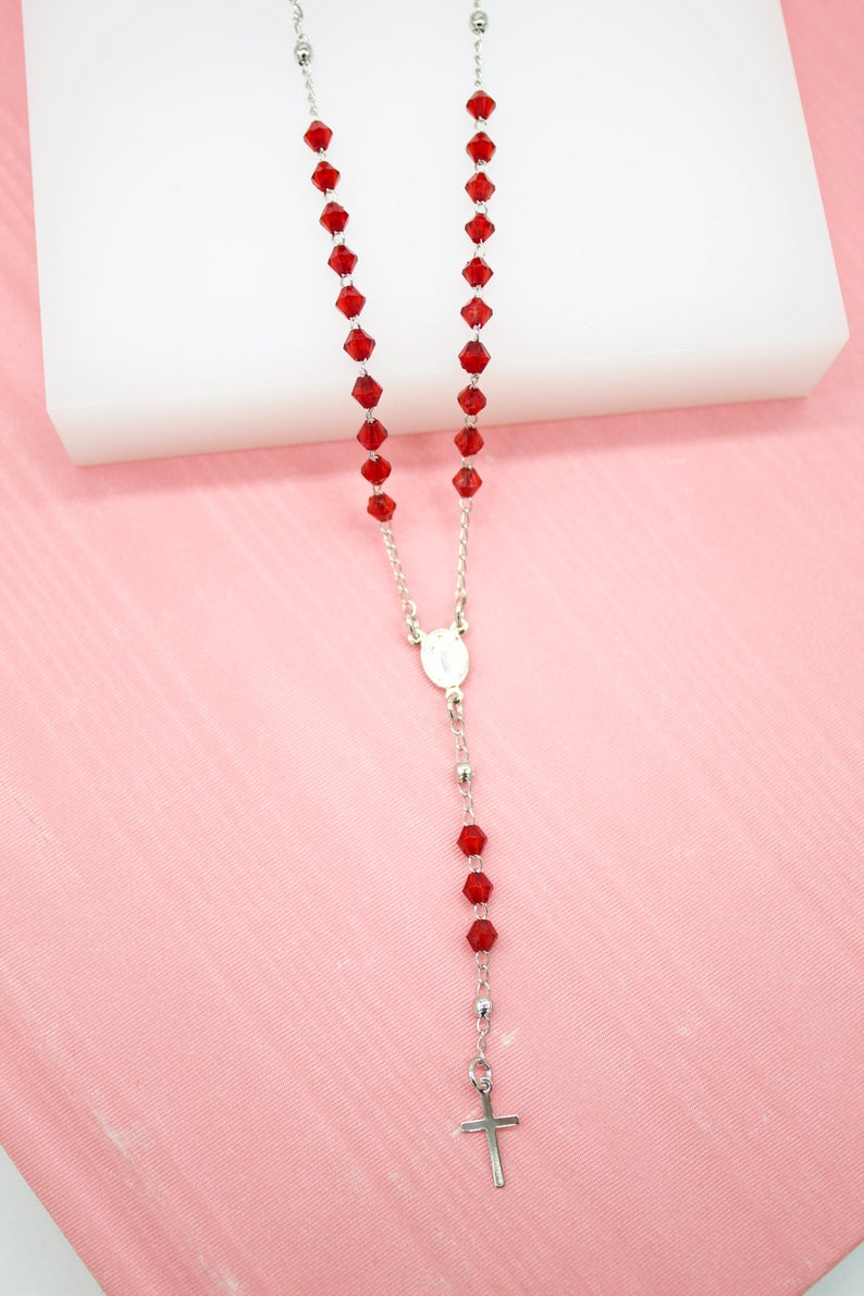 A delicate silver rosary featuring vibrant red crystal beads rests against a soft pink backdrop.