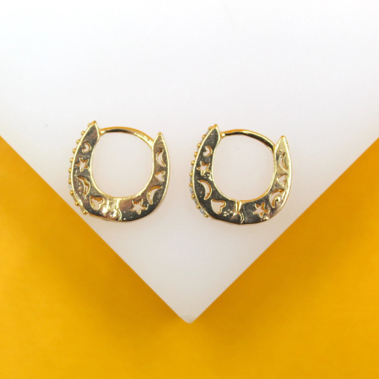 A pair of gold horseshoe huggie hoop earrings featuring cutout stars and moons rests on a white display surface.