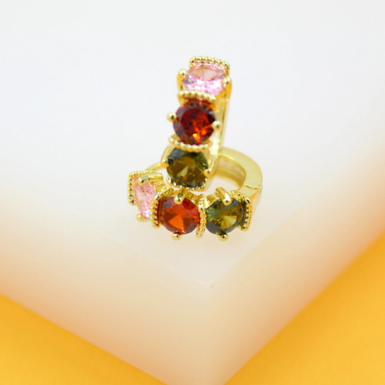 A pair of gold huggie earrings sparkles with multicolored cubic zirconia stones in pink, red, and green.