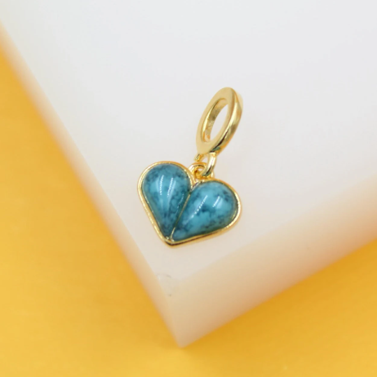 A gold-rimmed, blue turquoise heart charm rests against a white and yellow background.