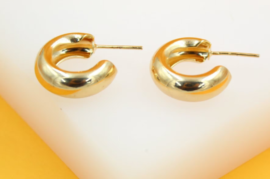 A pair of thick gold hoop earrings rests on a white display surface.