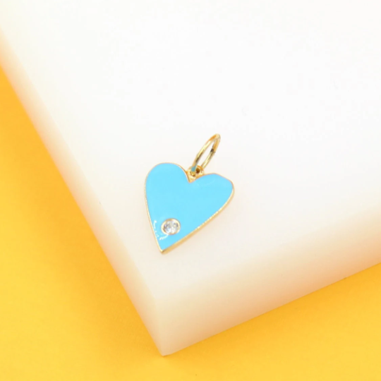 A gold heart pendant featuring bright blue enamel and a sparkling cz stone rests on a white surface.