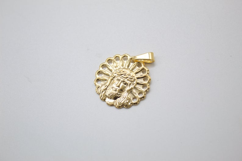 A gold Jesus pendant rests on a neutral surface, showcasing intricate details of the face and crown of thorns.
