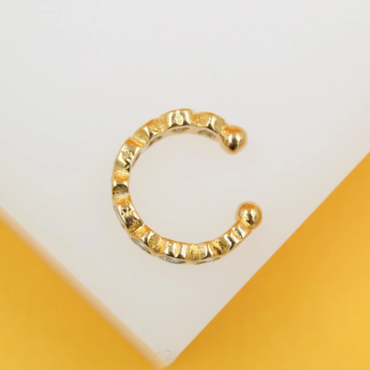 A textured gold-plated ear cuff rests on a white display surface with a yellow accent.