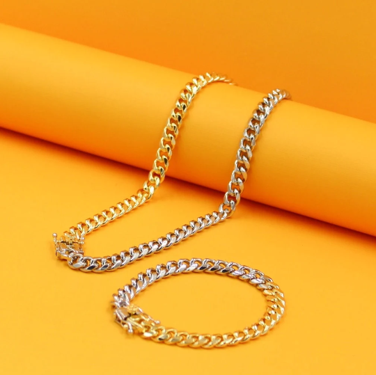 A matching two-tone gold and silver Miami Cuban link chain and bracelet set rests on a vibrant orange surface.