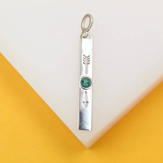 A silver bar pendant features an engraved arrow design and a round green gemstone against a white and yellow background.