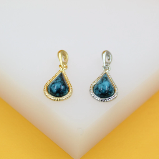 Two teardrop-shaped turquoise stone pendants display gold and silver settings on a white display block.