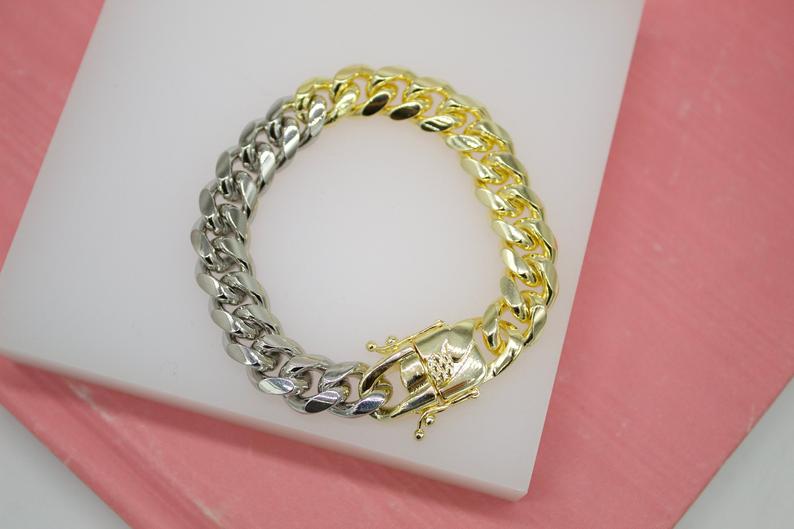 A two-tone cuban link bracelet rests on a white display stand against a pink background.