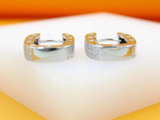 A pair of silver hoop earrings adorned with sparkling cubic zirconia stones rests on a white display surface.