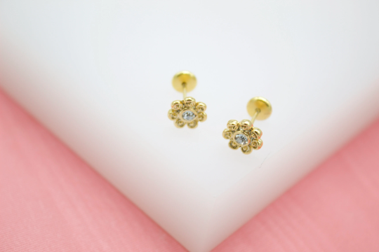 A pair of gold flower stud earrings featuring central cubic zirconia stones rests neatly on a white and pink display block.