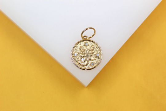A gold zodiac charm features a detailed Scorpio constellation design accented with small sparkling stones.