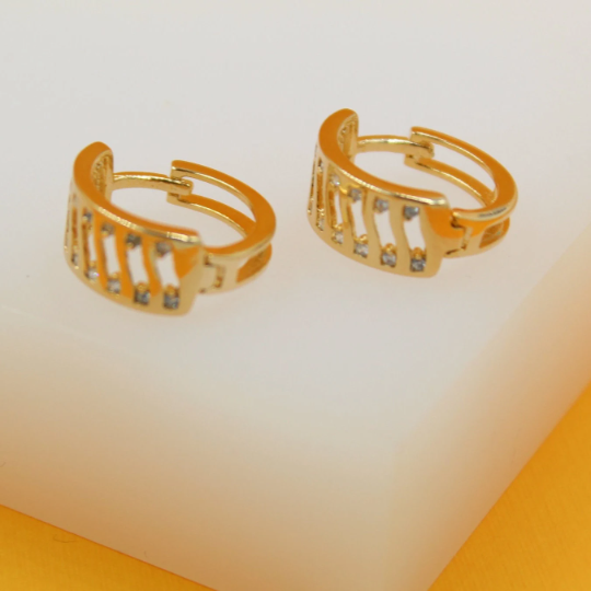 A pair of gold hoop earrings with sparkling stone accents rests on a clean white display surface.